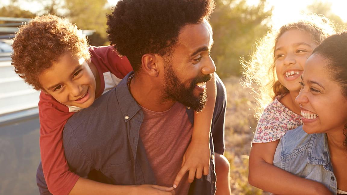 happy parents giving kids piggyback ride outdoors