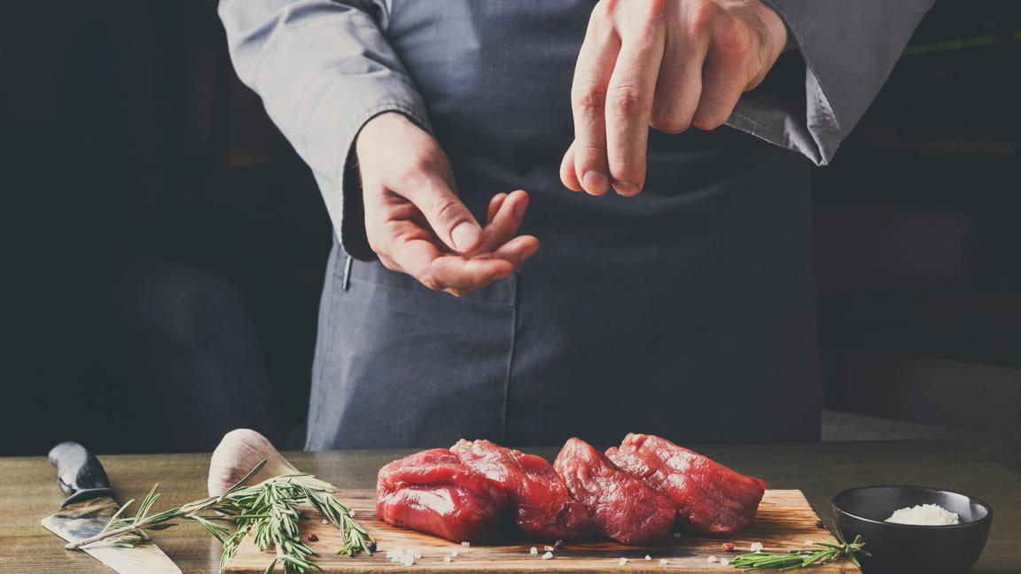 man's hands adding salt to meat while cooking